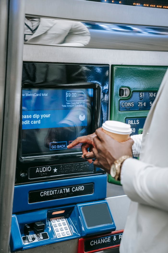 Close-up of a person using a subway ticket machine with a credit card and coffee cup.